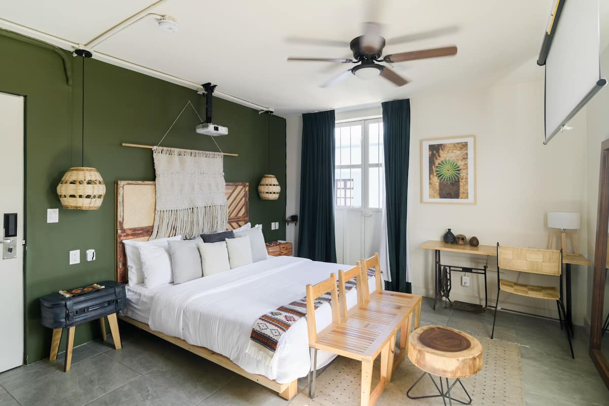 A bedroom with a bed, wooden chairs, a desk, and a ceiling fan.