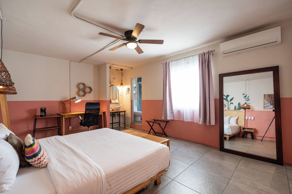 A bedroom with a bed, a desk, a chair, a mirror, and a ceiling fan.