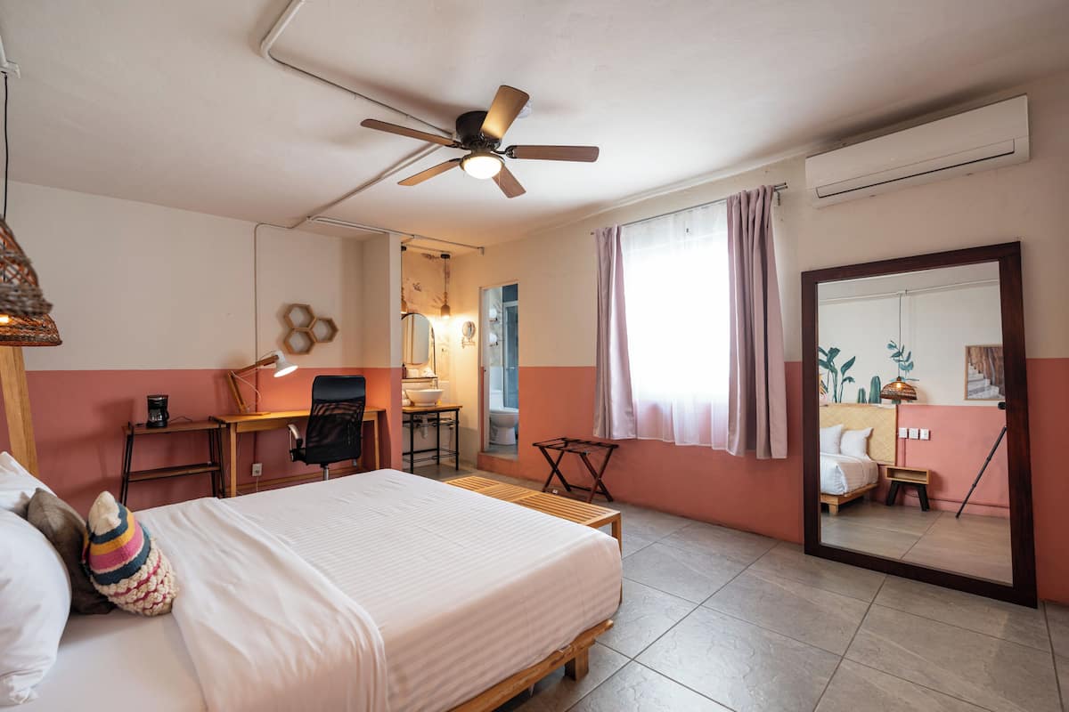 A bedroom with a bed, a desk, a chair, a mirror, and a ceiling fan.