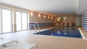 Une piscine intérieure avec un sol carrelé, des chaises longues blanches et une fresque murale.