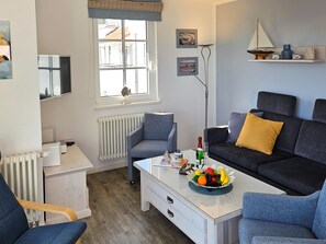 Una sala de estar moderna con un sofá, sillones, una mesa de centro con fruta, un radiador, una ventana con vistas y obras de arte en la pared.