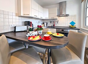 Cocina moderna con armarios blancos, extractor de acero inoxidable y comedor con una mesa redonda y sillas.