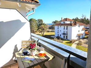 Un balcón con una mesa, una planta en maceta y vistas a un edificio blanco de techo rojo.
