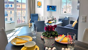 Un salon moderne comprenant un coin repas, de grandes fenêtres, un téléviseur à écran plat et une vue sur les bâtiments environnants.