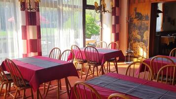 Un espace repas avec des tables disposées pour accueillir quatre personnes, des chaises en bois et une vue sur l’extérieur grâce à de grandes fenêtres.