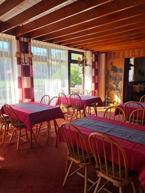 A dining area with tables set for four, wooden chairs, and a view of the outdoors through large windows. - Double room no. 22 - Waldpension Rabeneck (Waischenfeld)