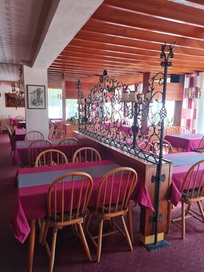 Ein Restaurant mit Holztischen und -stühlen, einem dekorativen Metallteiler und gerahmten Kunstwerken an den Wänden.