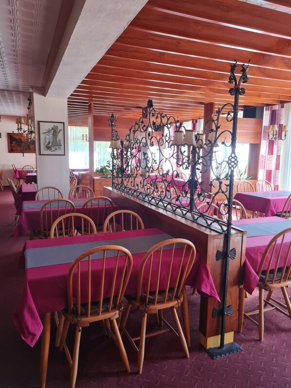 Un restaurant avec des tables et des chaises en bois, un paravent décoratif en métal et des œuvres d’art encadrées accrochées aux murs.