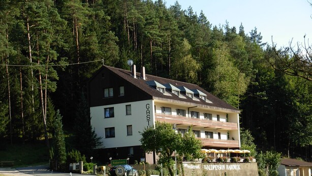 Un bâtiment à deux étages, sur lequel on peut lire les inscriptions « GASTHOF » et « RABENECK », indiquant qu’il s’agit d’une maison d’hôtes ou d’un hôtel.