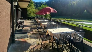 Une terrasse extérieure avec des tables et des chaises, un parasol rouge et une vue sur une rivière et une forêt.