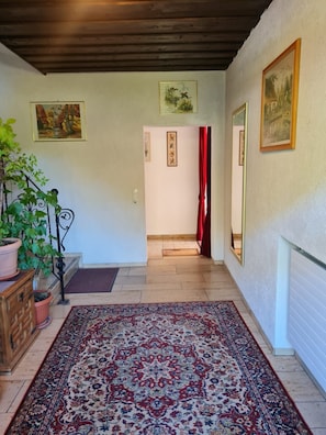 A hallway with a patterned rug, wooden furniture, and framed artwork on the walls. - Double room no. 22 - Waldpension Rabeneck (Waischenfeld)