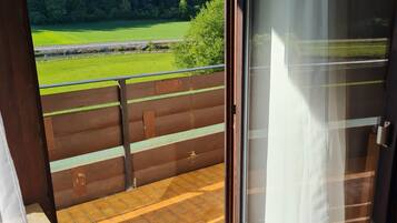 Ein Zimmer mit einer Schiebetür, die auf einen Balkon mit Blick auf einen Wald und ein grünes Feld führt.