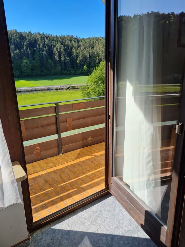 A room with a sliding glass door leading to a balcony with a view of a forest and a green field. - Double room no. 22 - Waldpension Rabeneck (Waischenfeld)