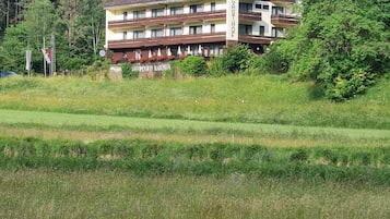 Ein mehrstöckiges Gebäude mit Balkonen, umgeben von einer grünen Wiese und bewaldeten Hügeln.
