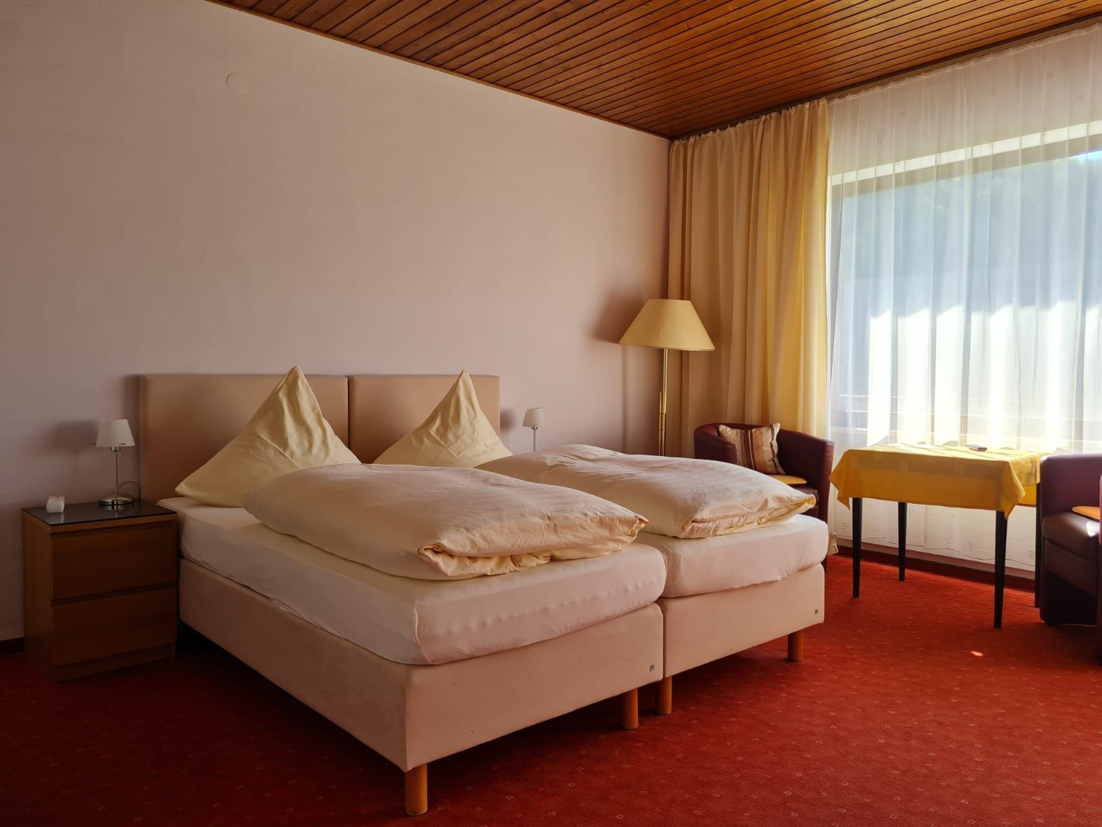 Une chambre d’hôtel avec un lit, des tables de chevet, une lampe, une chaise et une petite table.