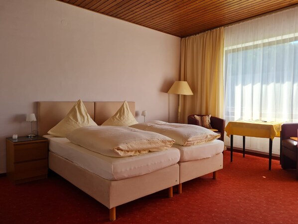 Hotellihuone, jossa on sänky, yöpöydät, lamppu, tuoli ja pieni pöytä.