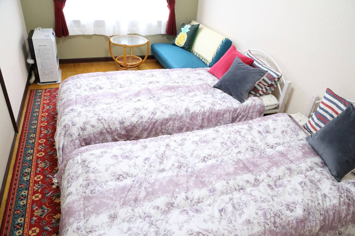 Una habitación con dos camas, una mesita redonda pequeña, un sofá y un calentador.