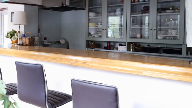 Une cuisine moderne avec un plan de travail en bois, deux chaises de bar noires et un meuble encastré doté de portes en verre.