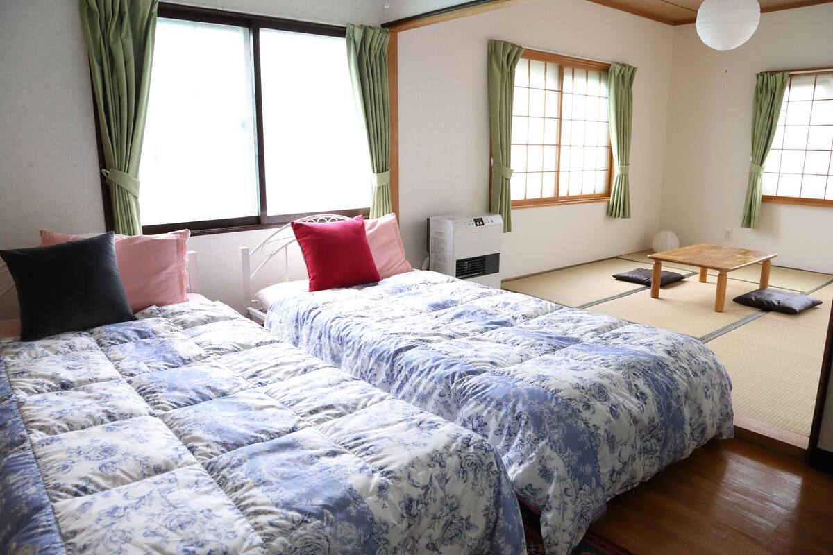 Una habitación tradicional japonesa con suelo de tatami, dos esteras de tatami, una mesa baja de madera y una cama futón con ropa de cama floral.