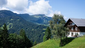 A mountain landscape with a wooden house featuring a balcony and a view of the valley.