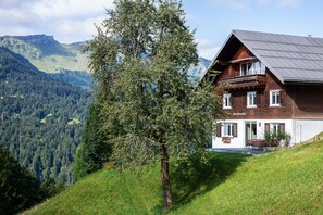 Een chalet met twee verdiepingen, een schuin dak, een balkon en uitzicht op een bebost dal.
