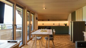 A modern kitchen with a dining area, wooden flooring, and large windows.