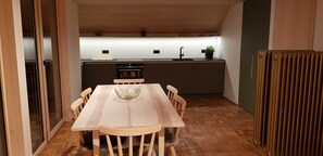 Un coin repas avec une table et des chaises en bois, une cuisine à l’arrière-plan et un radiateur sur la droite.