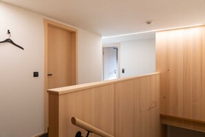 A modern interior with a wooden staircase, a hanging garment rack, and a door leading to another room.