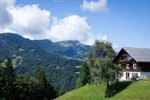 Un paysage de montagne avec une maison en bois dotée d’un balcon et offrant une vue sur la vallée.