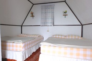 Una habitación con dos camas, cada una con una colcha a cuadros, una ventana con cortinas estampadas y dos estantes en la pared con flores.