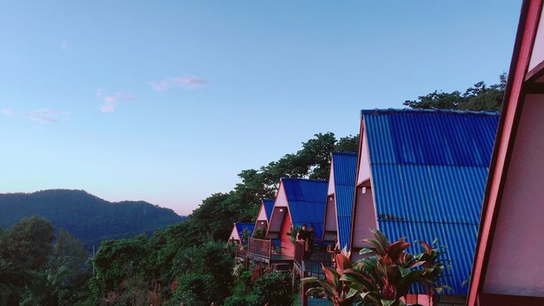 A row of blue-roofed buildings with a mountainous backdrop. - Ukrist Farm Hill Resort (Thoeng)