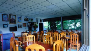 A dining area with a large wooden table and chairs, framed pictures on the walls, and large windows with a view of trees. - Ukrist Farm Hill Resort (Thoeng)