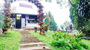 A building with a sign in a foreign language, surrounded by lush greenery and a stone staircase leading up to the entrance. - Ukrist Farm Hill Resort (Thoeng)
