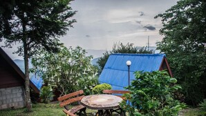 A rustic outdoor seating area with a wooden table and benches, surrounded by lush greenery and a blue-roofed structure. - Ukrist Farm Hill Resort (Thoeng)