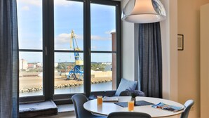 Une chambre moderne dotée d’une grande fenêtre, d’une table à manger avec des chaises, d’une lampe et donnant sur un chantier de construction.