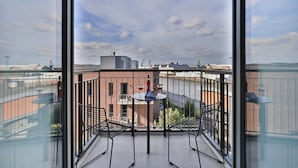 Un balcon donnant sur un paysage urbain, une table avec deux chaises et un livre.