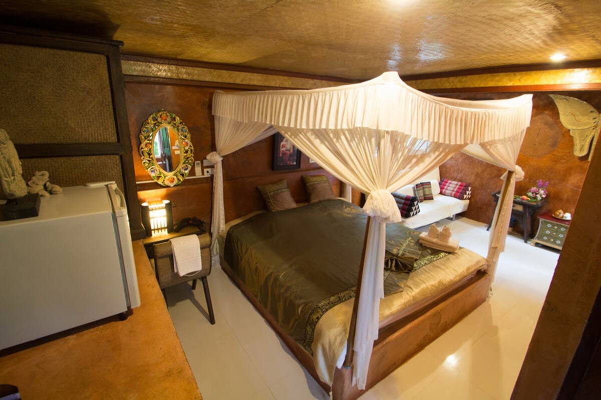 A four-poster bed with a canopy, a bedside table with a lamp, a mirror on the wall, and a small dresser with a mirror.