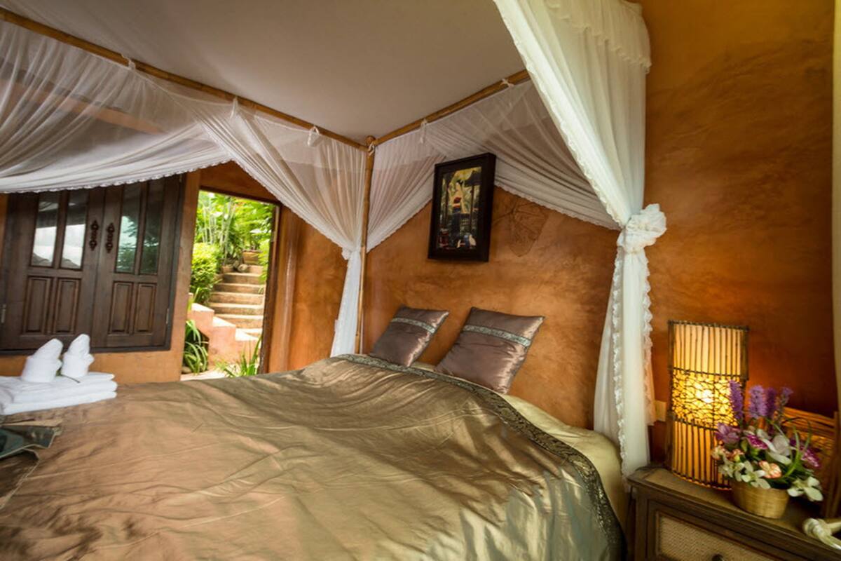 A bedroom with a large bed, a nightstand with a lamp, and a window with curtains.