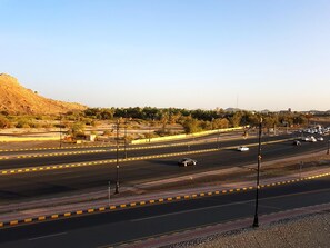 A multi-lane road with vehicles, a pedestrian walkway, and a hilly landscape in the background. - Tanuf Residency Hotel (Nizwa)