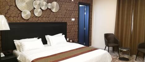 Ein Hotelzimmer mit einem großen Bett, einem Nachttisch, einem Sessel und einer Wand mit geometrischem Muster.
