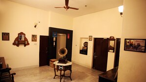 A spacious room with a ceiling fan, a door with a sign, a small table with a gramophone, and a framed picture on the wall. - Hotel Ajit Mansion (Jodhpur)