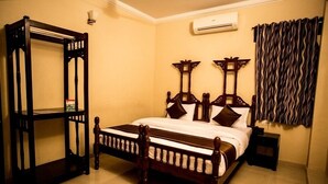 A bedroom with a wooden bed, a nightstand, a wall-mounted shelf, and a patterned curtain. - Hotel Ajit Mansion (Jodhpur)