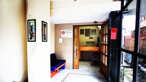 A reception area with a wooden desk, a blue bench, and a sign indicating CCTV surveillance. - Hotel Ajit Mansion (Jodhpur)
