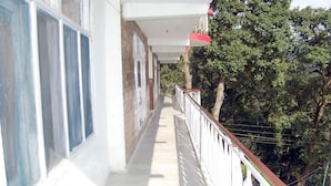 A balcony with a white railing, a red light fixture, and a view of trees. - Hotel Goher (Dalhousie)
