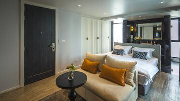 A modern bedroom with a large bed, a sofa, a small table with a vase, and a dark door.