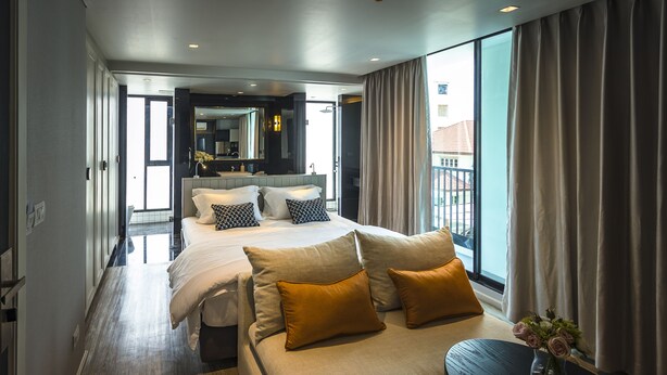 Una habitación de hotel moderna con una cama grande, un sofá y una mesita con un jarrón de flores.