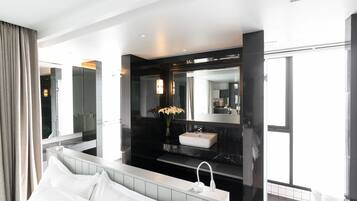 A modern hotel room with a large bed, a bathroom with a vanity, and a large mirror.
