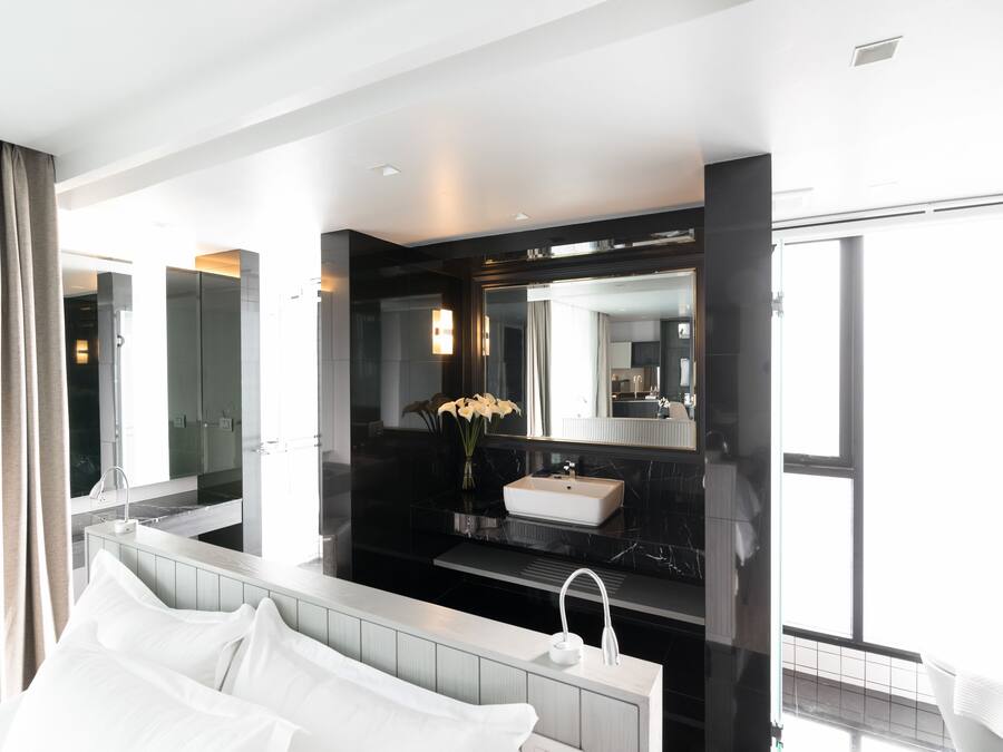 A modern hotel room with a large bed, a bathroom with a vanity, and a large mirror.