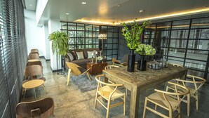 Un interior moderno con una mesa de comedor de madera, sillas de mimbre, un sofá y plantas en macetas.