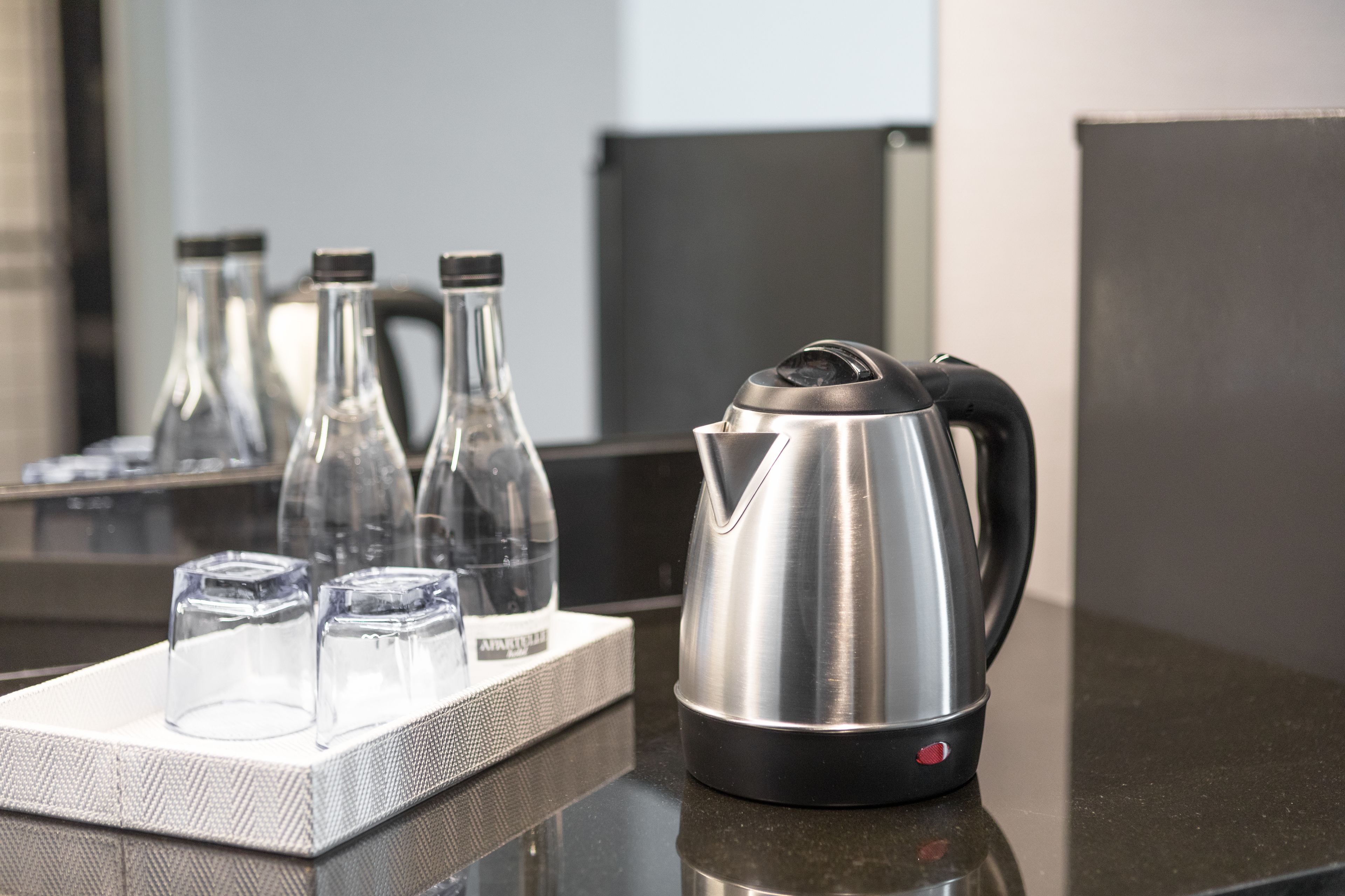 A stainless steel kettle on a countertop with a tray of glasses and ice cubes.